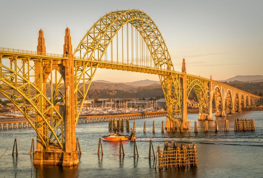 A fishing trawler returns to port at the end of the day and passes beneath Yaquina Bay Bridge, Newport, Oregon.